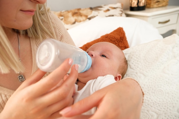 Mama karmi noworodka butelką, w której w tle świeci słońce