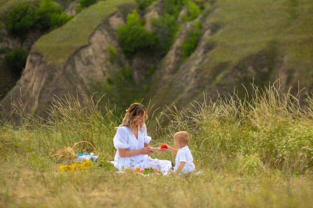 Mama karmi swojego syna. Piękna dziewczyna z dzieckiem w tej dziedzinie. Dziecko z matką je. Dzień Matki. Matka i syn. Kobieta w polu z dzieckiem. Dzień Ochrony Dzieci.