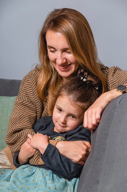 Mama mocno przytula córkę, siedząc na przytulnej domowej kanapie