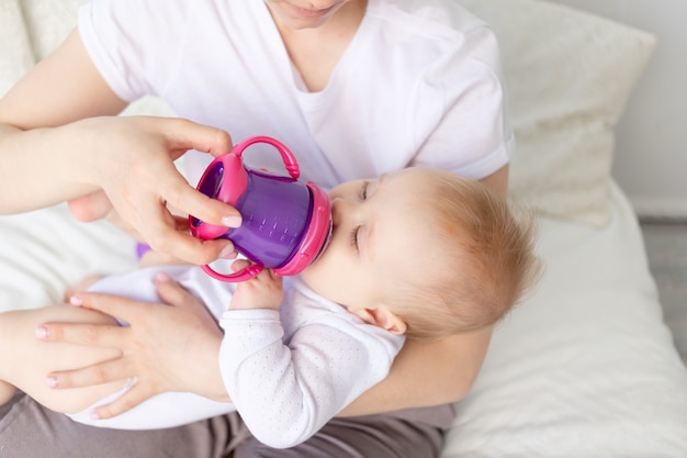 Mama Pije Lub Karmi Dziecko Butelką Na Białym łóżku W Domu, Koncepcja Jedzenia Dla Niemowląt