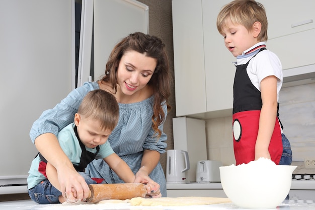 Mama pomaga młodym synom wyrabiać ciasto na kuchennym stole