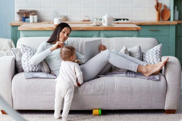 Mama pracuje przy laptopie w domu, podczas gdy jej dziecko się bawi