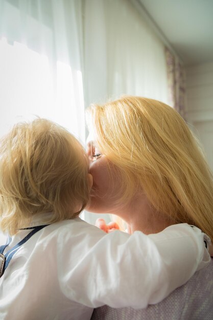 Mama przytula i całuje dziecko stojące przy oknie