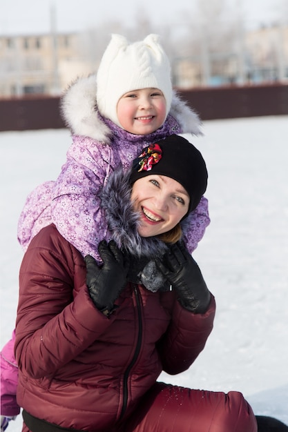 Mama przytula swoją piękną córkę zimą na lodowisku.