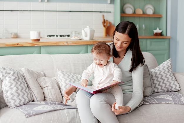 Mama siedzi na kanapie z dzieckiem, czyta książkę i ogląda jasne zdjęcia