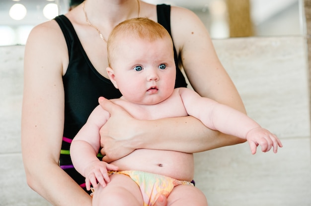 Mama Trzyma Córeczkę 6 Miesięcy, Dziecko W Ramionach Na Basenie. Pierwsza Lekcja Pływania. Przygotuj Się Do Nurkowania. Zaskoczony. Z Otwartymi Ustami. Rude Włosy. Zbliżenie