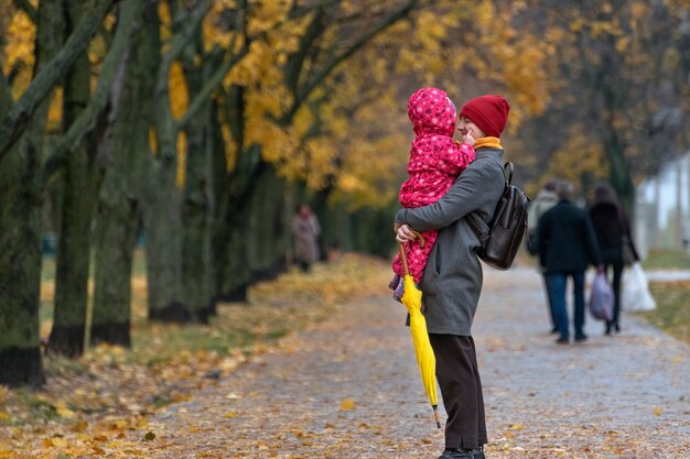 Mama trzyma dziecko w ramionach na tle jesiennego parku. Spacery z dziećmi.