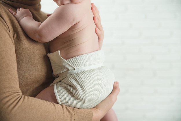 mama trzyma dziecko w ramionach w bawełnianych pieluchach wielokrotnego użytku