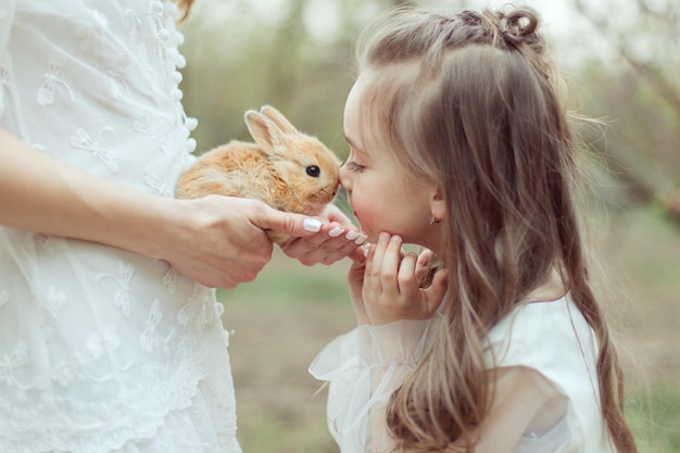 Mama trzyma w rękach małego królika Córka całuje królika