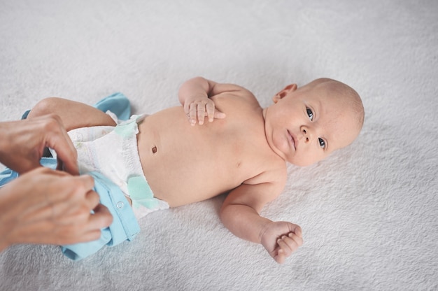 Mama ubiera uroczy emocjonalny zabawny noworodek małego chłopca w niebieski kombinezon Infant baby Nursery