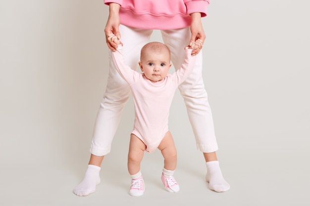 Mama Uczy Córkę Chodzić, Bez Twarzy Kobieta W Białych Spodniach, Trzymająca Dziecko Za Rączki I Chodząca Po Domu Pod Białą ścianą, Dziecko Patrzy W Kamerę I Lubi Chodzić.