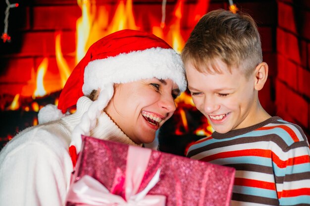 Mama w sylwestrowej czapce daje synowi prezent na tle kominka