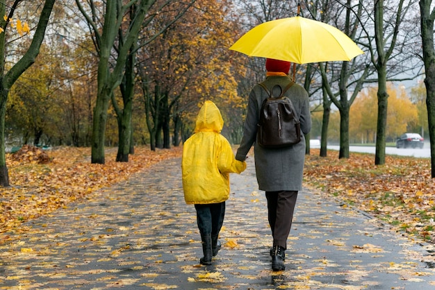 Mama Z Dużym żółtym Parasolem I Synem W żółtej Kurtce Chodzą W Jesiennym Parku Widok Z Tyłu