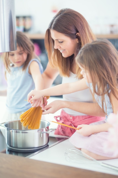 Mama z dwiema córkami młodych bliźniaków w kuchni gotowanie spaghetti.