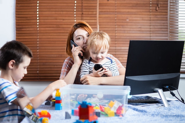 Mama z dwoma małymi chłopcami na kolanach próbuje się śmiać w domu.