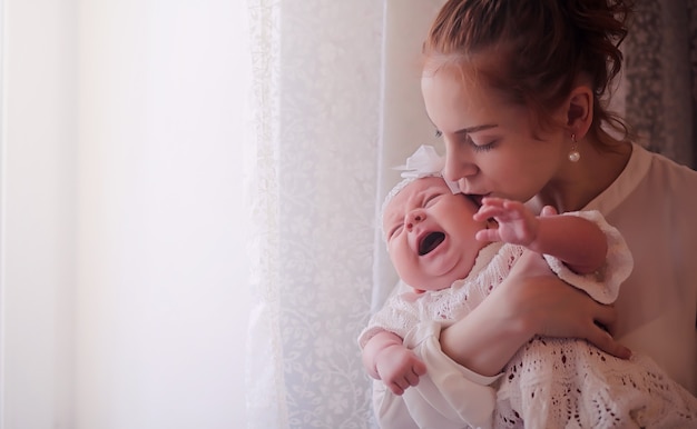 Mama z noworodkiem w ramionach. Dziewczyna trzyma dziecko przed oknem. Noworodek na rękach matki.