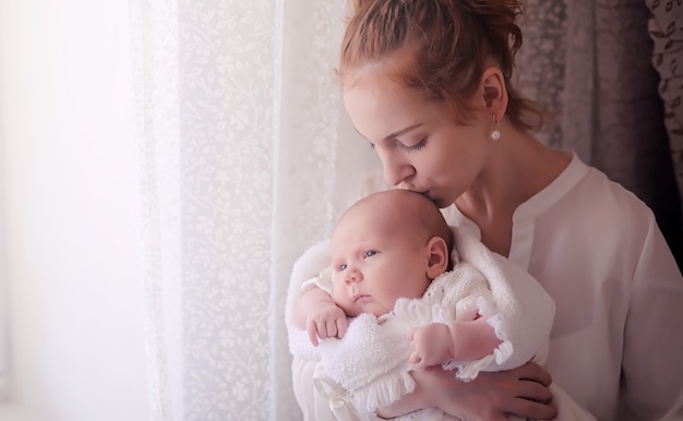 Mama z noworodkiem w ramionach. Dziewczyna trzyma dziecko przed oknem. Noworodek na rękach matki.