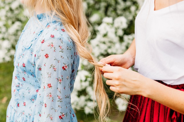 Mama zaplata włosy dziewczynki w naturze, lato i wiosna, blond włosy, kobiece dłonie