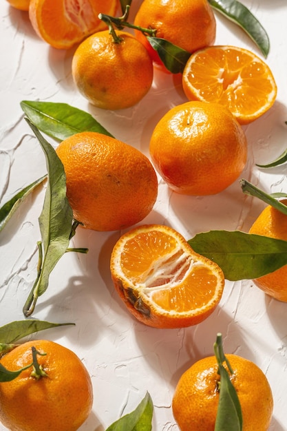 Mandarynki (pomarańcze, mandarynki, klementynki, owoce cytrusowe) o zielonych liściach. Nowoczesne twarde światło, ciemny cień. Białe tło szpachlowe, kreatywne mieszkanie leżące, z bliska