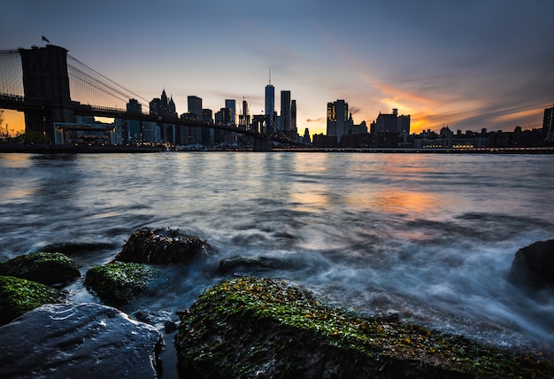 Manhattan skyline z Brooklyn Bridge wieczorem. Skały i kamienie na brzegu East River