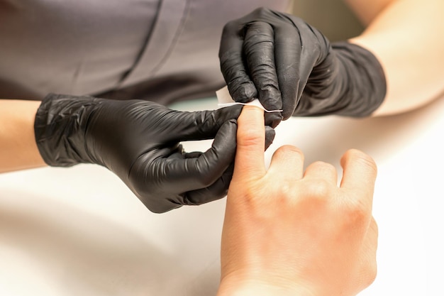Zdjęcie manikiurzystka kończy zabieg polerowania i czyszczenia na czerwono paznokci wacikiem wacikiem w gabinecie kosmetycznym z bliska