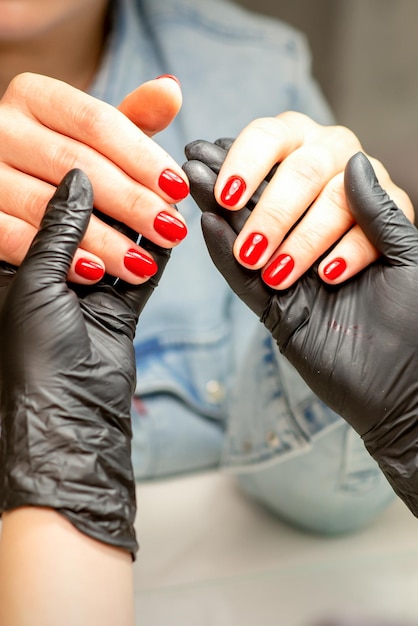 Manikiurzystka trzyma piękne młode kobiece dłonie pokazujące gotowy czerwony polski manicure w salonie paznokci