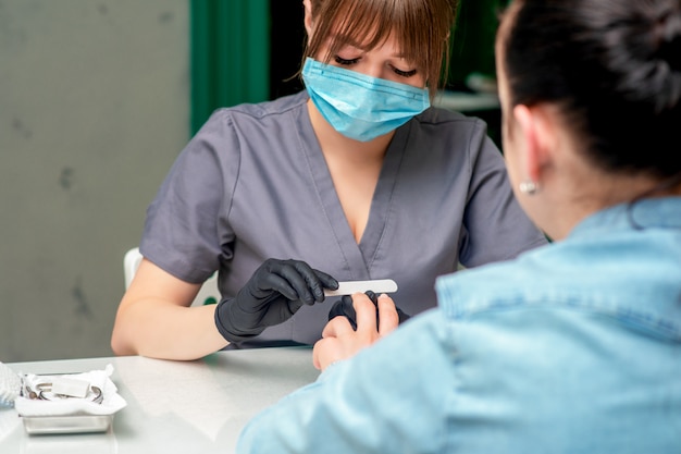 Manikiurzystka wykonuje manicure pilnikiem do paznokci.