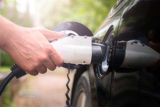 Zdjęcie mans ręcznie wkładając wtyczkę ładowarki do samochodu elektrycznego w zielonym tle środowiska. nowy pojazd energetyczny, nev, jest ładowany energią elektryczną. ekologia, współczesne samochody