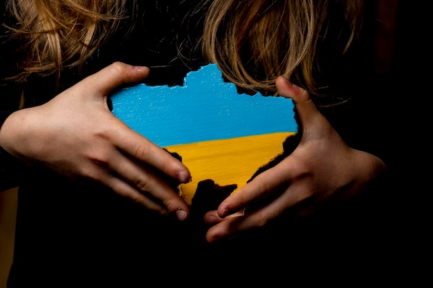 Zdjęcie mapa ukrainy wyrzeźbiona z drewna i pomalowana na kolory ukraińskiej flagi w rękach dziewczyny na ciemnym tle