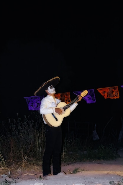 Zdjęcie mariachi w makijażu day of the dead brzdąka na gitarze pod neonem