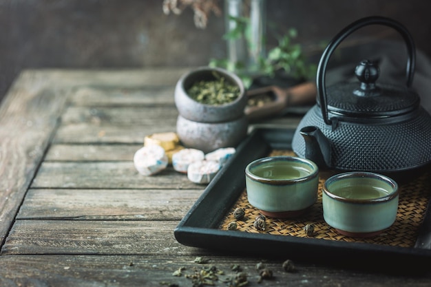 Martwa natura japońskiej zdrowej zielonej herbaty w małych filiżankach i czajniczku na ciemnym tle