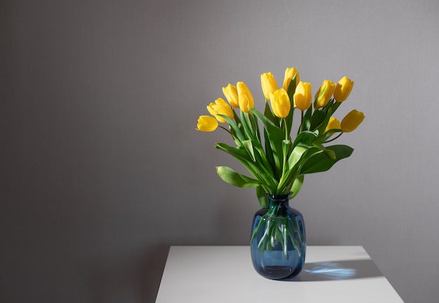 Martwa Natura Z Bukietem żółtych Tulipanów W Niebieskim Szklanym Wazonie Na Białym Stole. Wystrój Wnętrz Domu. Skopiuj Miejsce
