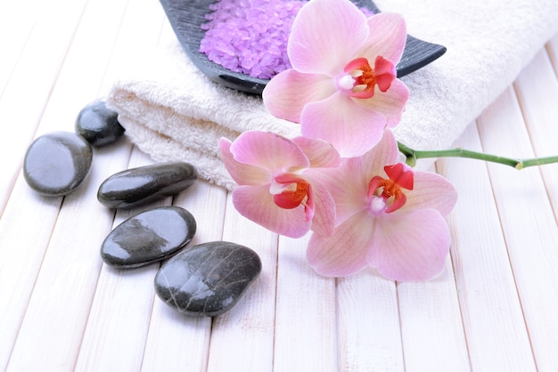 Martwa natura z pięknym kwitnącym kwiatem orchidei, ręcznikiem i miską z solą morską, na kolorowym drewnianym stole
