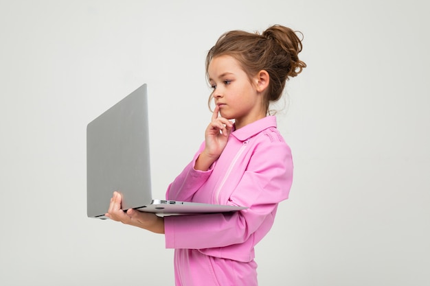 Marząca dziewczyna w różowym garniturze trzyma laptopa otwartego na białej ścianie