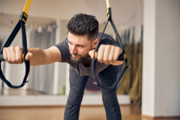 Zdjęcie marzycielski, elastyczny, krótkowłosy mężczyzna rasy kaukaskiej, wykonujący ćwiczenia z szeroko rozstawionymi stawami biodrowymi na siłowni