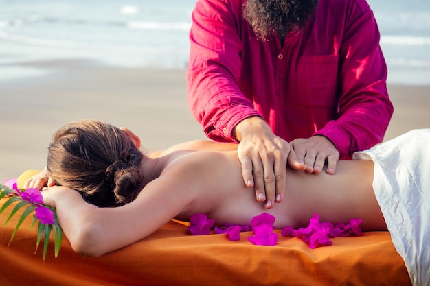 Masaż leczniczy na brzegu tropikalnego morza. Ajurwedyjski relaksacyjny masaż kobieta w salonie spa podczas masażu na wakacyjnej plaży. dziewczyna leżąc na stole zabiegowym