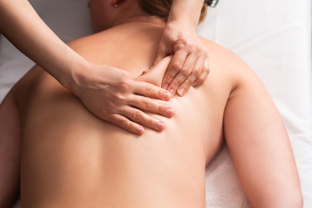 Masażysta masuje plecy i łopatki młodej kobiety na stole do masażu Koncepcja zabiegów spa masażu Zbliżenie
