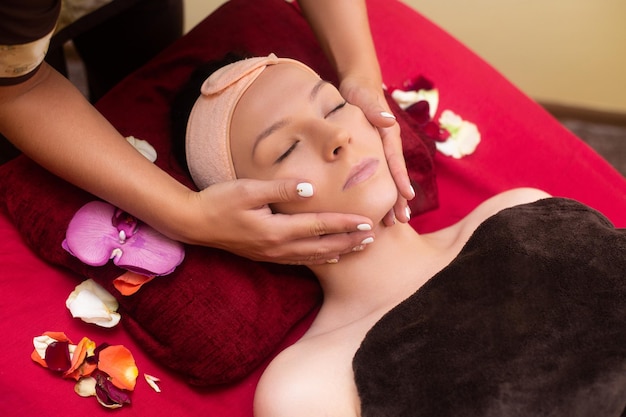 Masażystka w salonie kosmetycznym wykonuje masaż tajski na twarzy młodej dziewczyny
