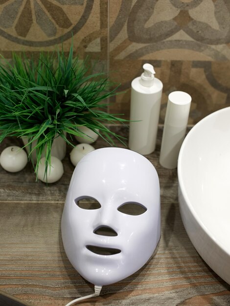 Zdjęcie maska led do terapii światłem na półce obok produktów do pielęgnacji skóry twarzy w łazience