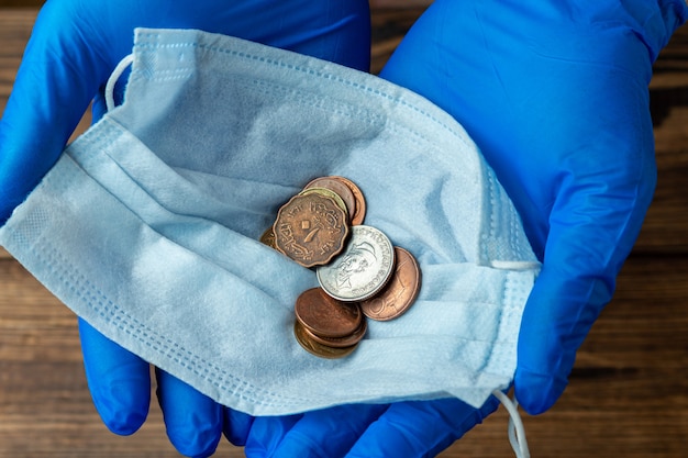 Maska ochronna z monetami w rękach w rękawiczkach medycznych