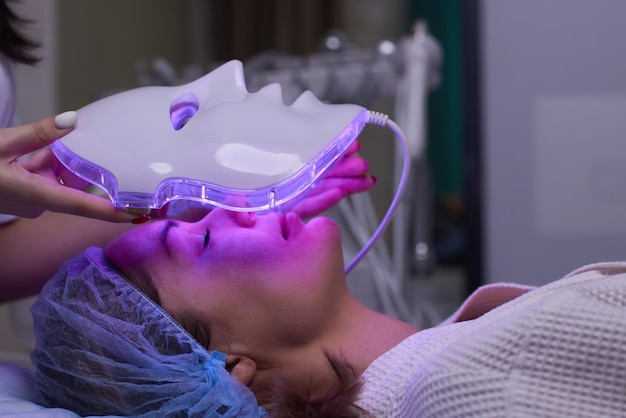 Maska przeciwstarzeniowa LED do pielęgnacji skóry twarzy w spa w zwolnionym tempie Kobieta leży na kanapie w specjalnej masce Nowoczesne technologie urody i zdrowia