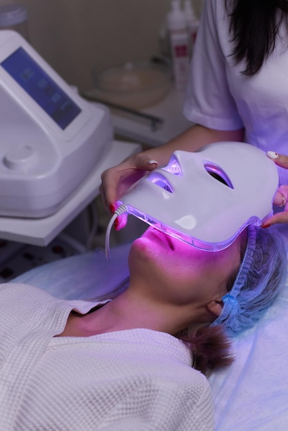 Maska przeciwstarzeniowa z oświetleniem led do pielęgnacji skóry twarzy w spa w zwolnionym tempie kobieta leży na kanapie w specyfikacji