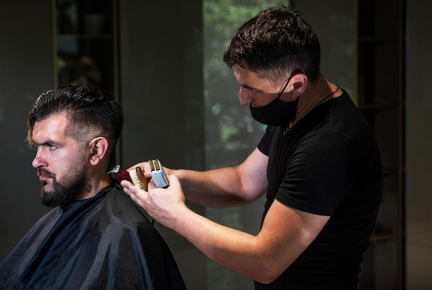 Master Barber robi fryzurę i stylizację za pomocą golarki elektrycznej dla mężczyzny Concept Barbershop