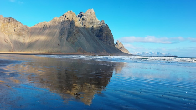 Masywny łańcuch górski spotykający ocean, piękne krajobrazy islandzkie z czarną piaskową plażą. Półwysep arktyczny Stokksnes z górami vestrahorn i wybrzeżem oceanu, zwiedzanie.