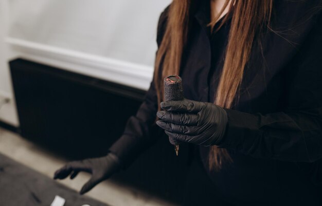 Maszynka do tatuażu w kobiecych dłoniach w czarnych rękawiczkach warsztat makijażu permanentnego tatuażu