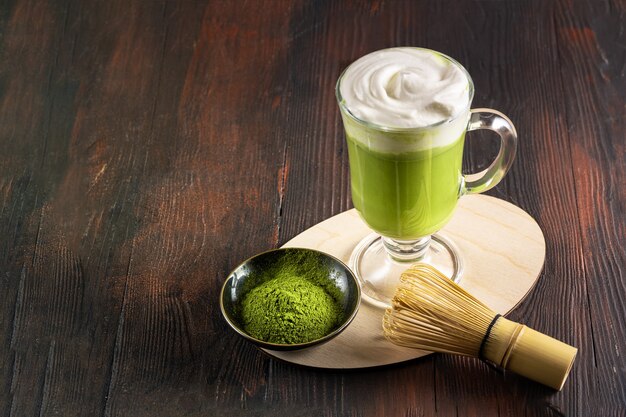 Matcha latte z kremową pianką w szklankach w pobliżu bambusowej trzepaczki i proszku matcha