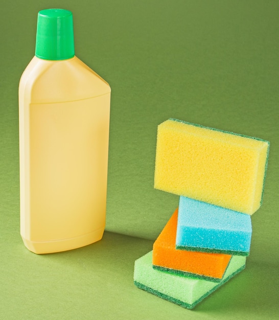 Materiały do czyszczenia domu Butelka z detergentem i wielobarwnymi gąbkami na zielonym tle