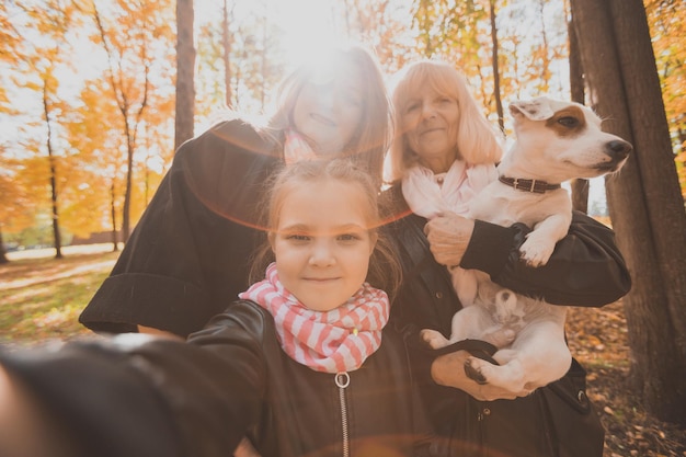 Matka, babcia i mała wnuczka z psem jack russell terrier biorąc selfie przez smartfon na zewnątrz w jesiennej przyrodzie. Koncepcja rodziny, zwierząt domowych i generacji