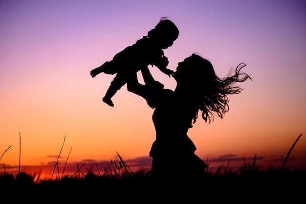 Matka bawi się z dzieckiem w ramionach pod promieniami zachodu słońca na łące