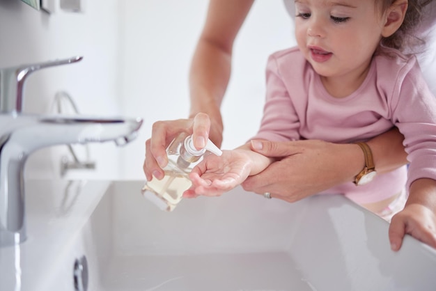 Matka czyści ręce dzieci mydłem w płynie odkażającym po tym, jak maluch miał brudne palce w zlewie Zdrowa pielęgnacja i mama sprzątanie i pomaganie młodej dziewczynie w higienie wellness w domu